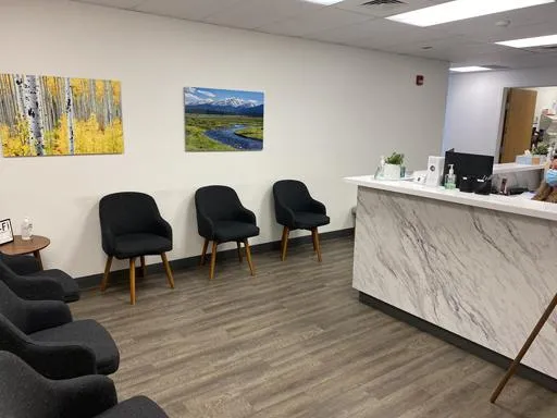 Modern dental office waiting room with black chairs, marble reception desk, and landscape artwork on walls.